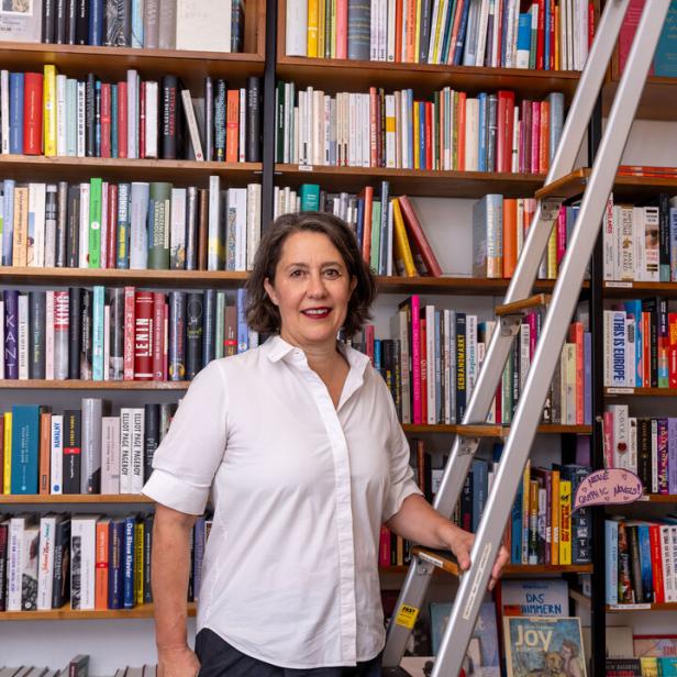 Eine Frau steht vor einem Bücherregal mit einer Leiter.