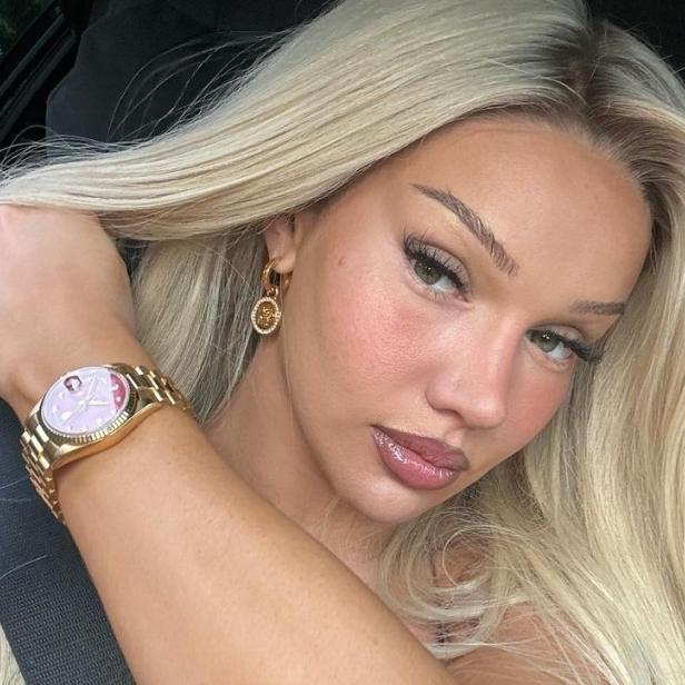 29-jährige Frau mit blonden langen Haaren und goldenem Schmuck posiert für ein Selfie im Auto.