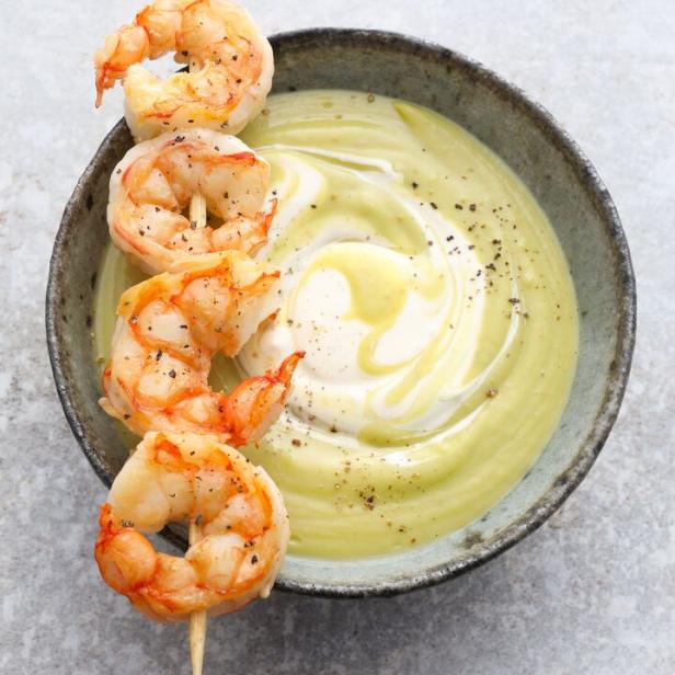 Ein Spieß mit Garnelen liegt auf einer Avocado-Limetten-Suppe.