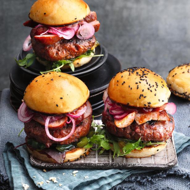 Drei Burger mit Wurst, roten Zwiebeln und Salat werden präsentiert.
