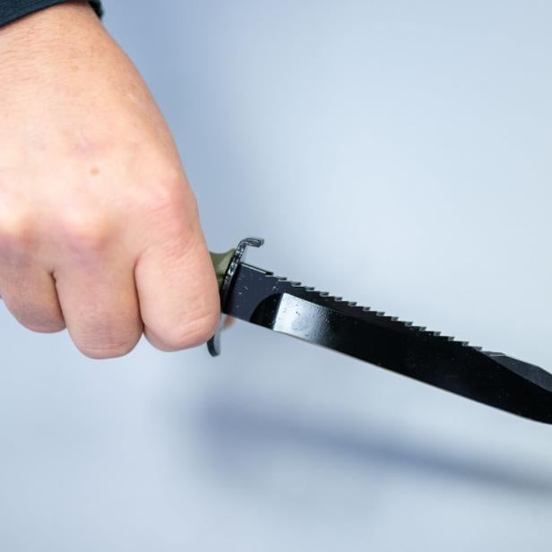 Eine Hand hält ein schwarzes Messer mit gezackter Klinge.
