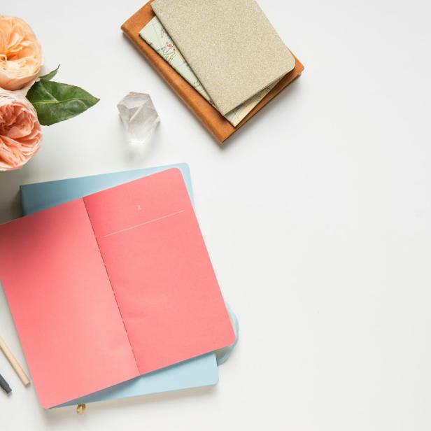 Rosen, Stifte und Notizbücher liegen auf einem weißen Tisch.