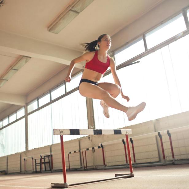 Sportlerin springt über eine Hürde in einer Halle.