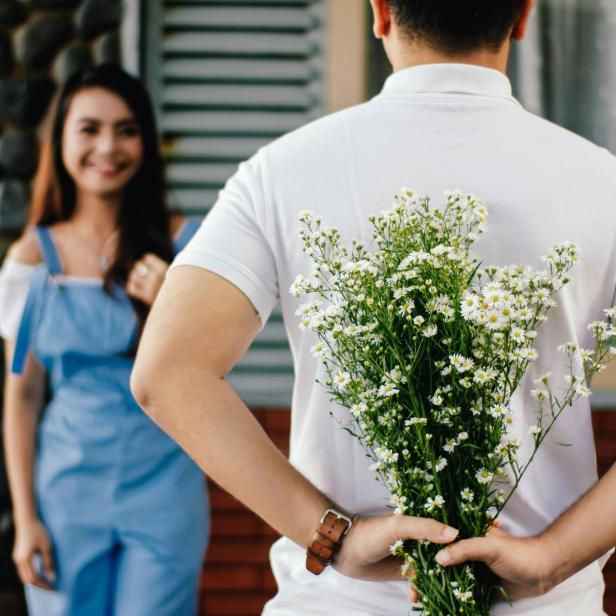 Ein Mann versteckt einen Strauß weißer Blumen hinter seinem Rücken für eine Frau.