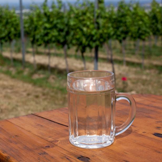 Ein Glas Weißer Spritzer steht auf einem Holztisch im Weinberg.