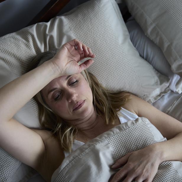 Eine Frau liegt im Bett und hält die Hand auf die Stirn.
