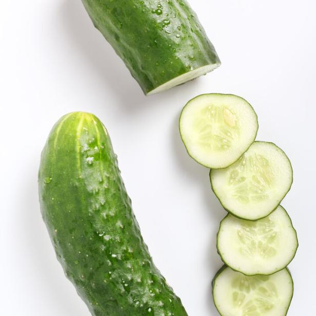Ein ganzer und ein angeschnittener, grüner Salatgurke liegen auf einem weißen Untergrund.
