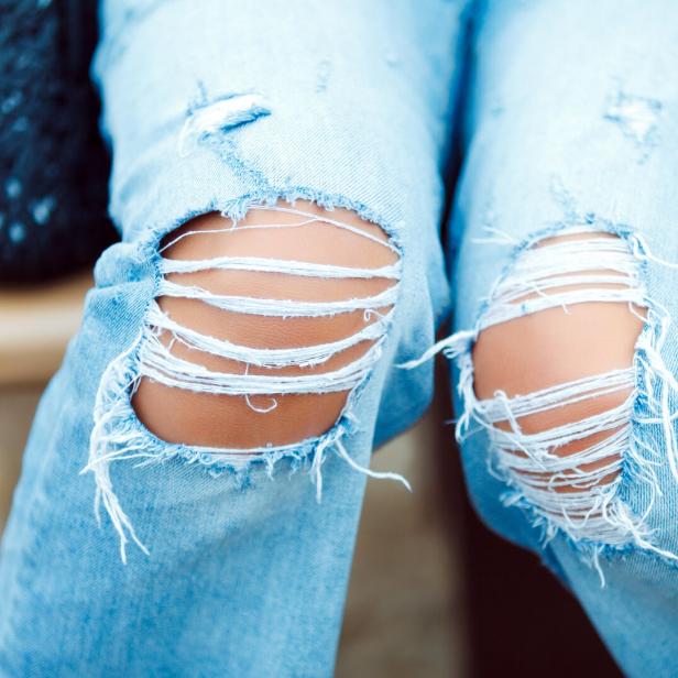 Nahaufnahme von zerrissenen Jeans an den Knien einer Person.