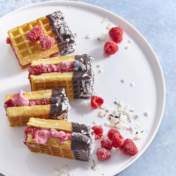 Waffel-Sandwiches mit Himbeerfüllung, Schokoladenglasur und Kokosraspeln auf einem Teller.