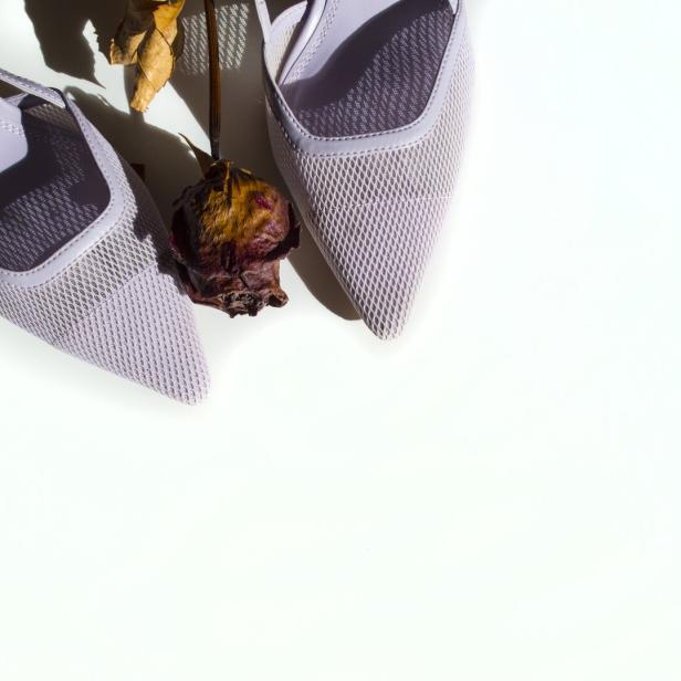 Ein Paar lila Kitten Heels mit einer verwelkten Rose auf einem weißen Hintergrund.