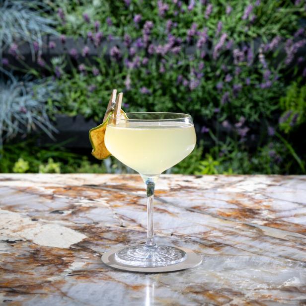 Ein Cocktail mit einer Birnenscheibe als Dekoration vor einem Hintergrund aus Lavendelbüschen.