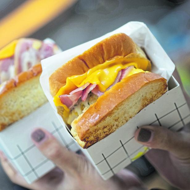 Zwei Egg-Drop-Toast-Sandwiches mit Käse und Speck werden in der Hand gehalten.