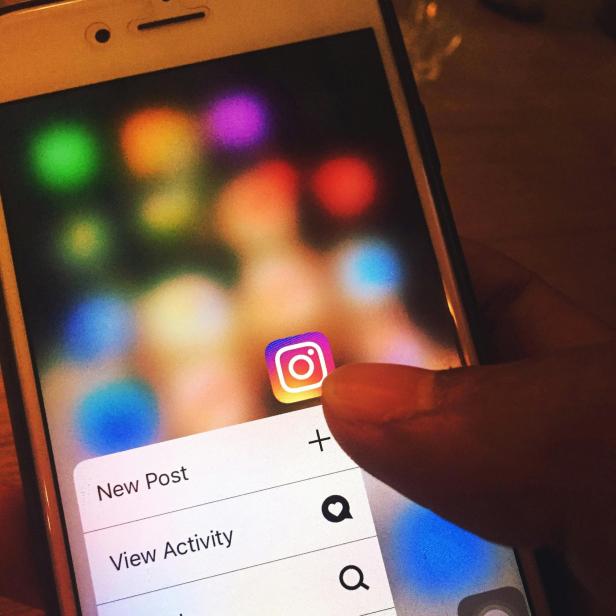 Ein Finger tippt auf das Instagram-Symbol auf einem Smartphone, es erscheinen Optionen wie „New Post“ und „View Activity“.