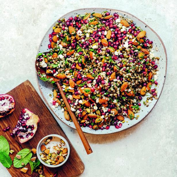 Ein Teller Linsen-Graupensalat mit Mandeln, Granatapfelkernen und Feta auf einem Tisch.