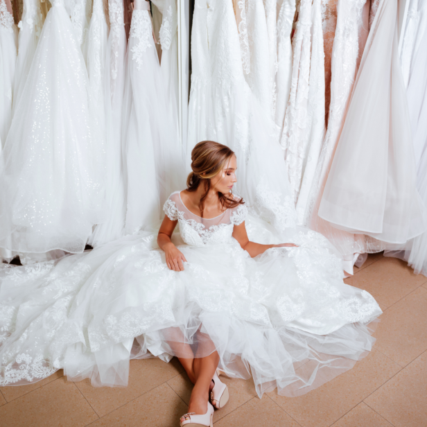 Eine Frau sitzt in einem Brautkleid vor einer Reihe von Hochzeitskleidern.