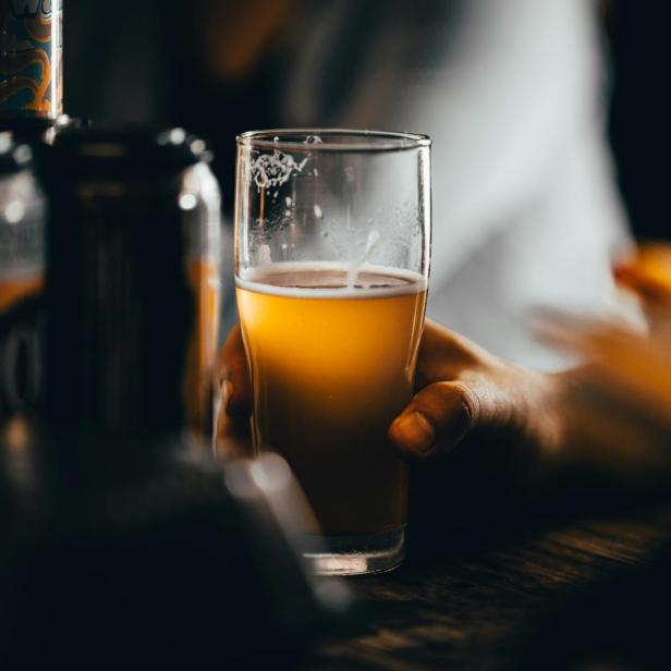 Eine Hand hält ein Glas Craft Beer vor einem dunklen Hintergrund.