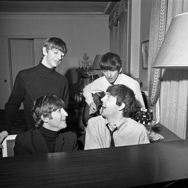 Die Beatles posieren mit Gitarre und Klavier in einem Raum.