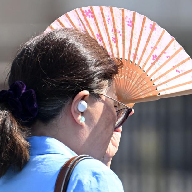 Sommerliche Hitze: Eine Frau schützt sich mit einem Fächer vor der Sonne.