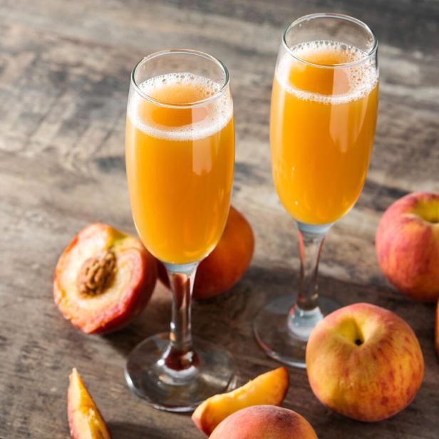 Zwei Gläser Bellini und Pfirsiche auf einem Holztisch.
