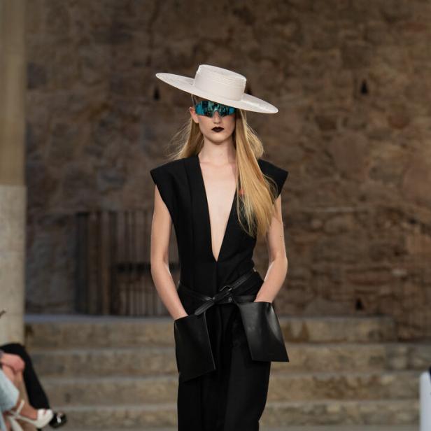 Ein Model in einem schwarzen Hosenanzug, Hut und futuristischer Brille auf dem Laufsteg bei Louis Vuitton.