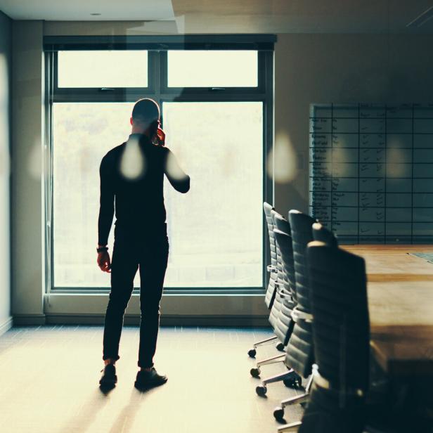 Rearview shot of a young businessman talking on a cellphone in an empty boardroom