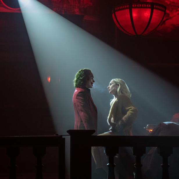 Der Joker im roten Anzug steht im Scheinwerferlicht mit Harley Quinn mitten in einem dunklen Gerichtssaal.