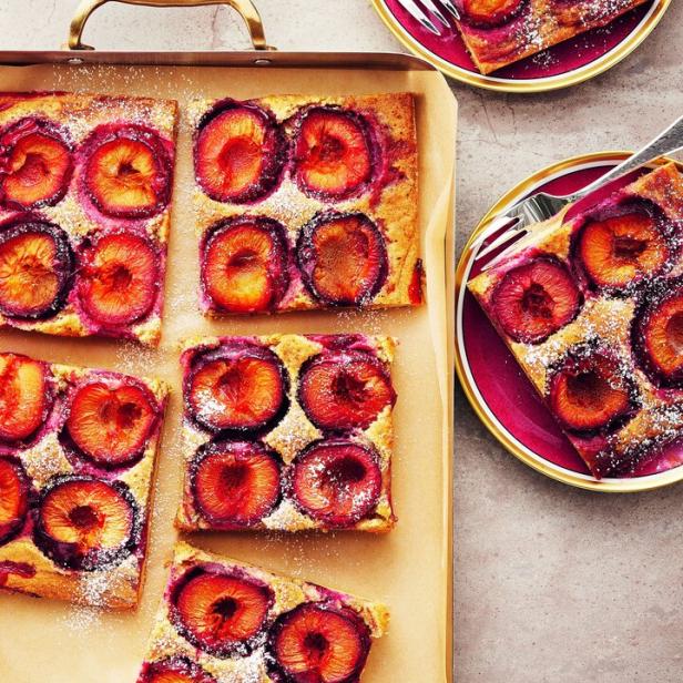 Zwetschgenkuchen, mit Puderzucker bestäubt, auf einem Backblech und Tellern.