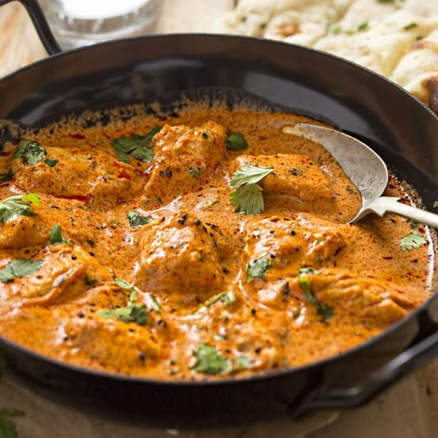 Ein Gericht mit Murgh Makhani, garniert mit Koriander, neben Naan-Brot.