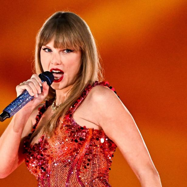 Taylor Swift singt in einem roten Paillettenkleid in ein glitzerndes Mikrofon.
