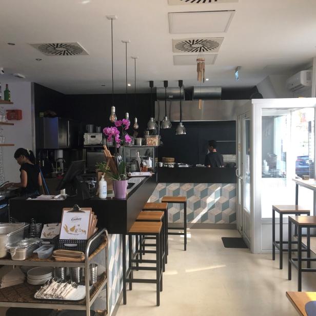 Innenansicht eines Restaurants mit Bar, Sitzgelegenheiten und einer Person, die im Hintergrund arbeitet.