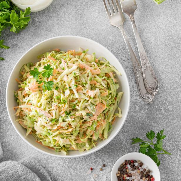 Ein Schüssel Krautsalat mit Karotten und Petersilie auf einem grauen Tisch.
