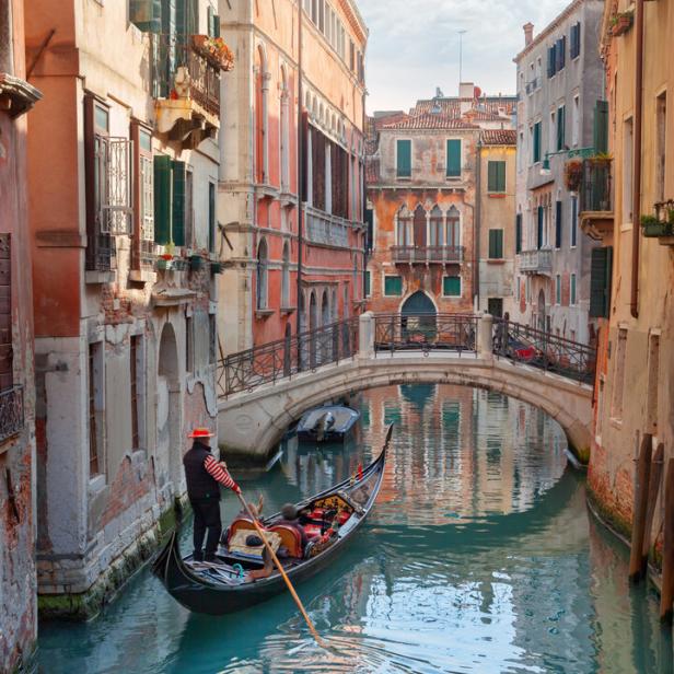 Ein Gondoliere steuert seine Gondel durch einen Kanal in Venedig.