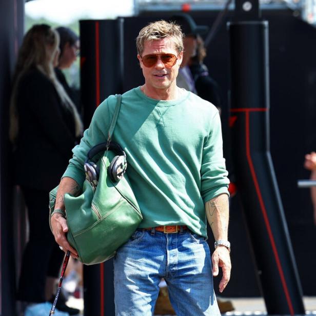 Brad Pitt mit Sonnenbrille, Jeans und grüner Tasche bei einem Formel-1-Rennen.