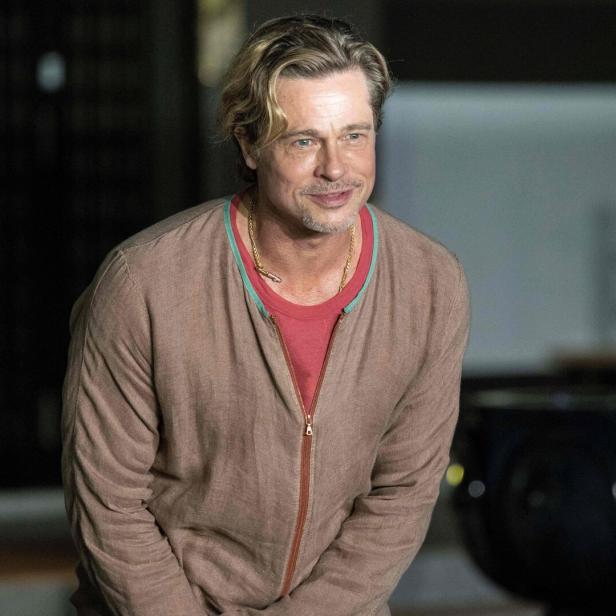 Brad Pitt lächelt in einem braunen Cardigan und einer goldenen Halskette.