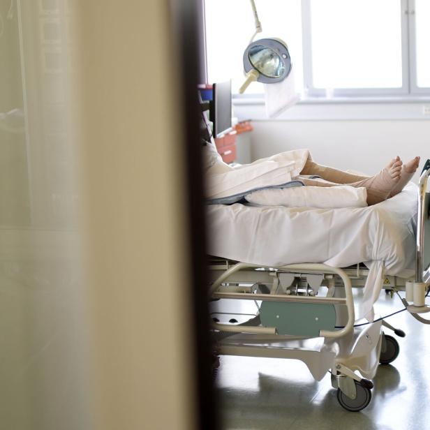 Eine Person liegt mit bandagierten Beinen in einem Krankenhausbett.