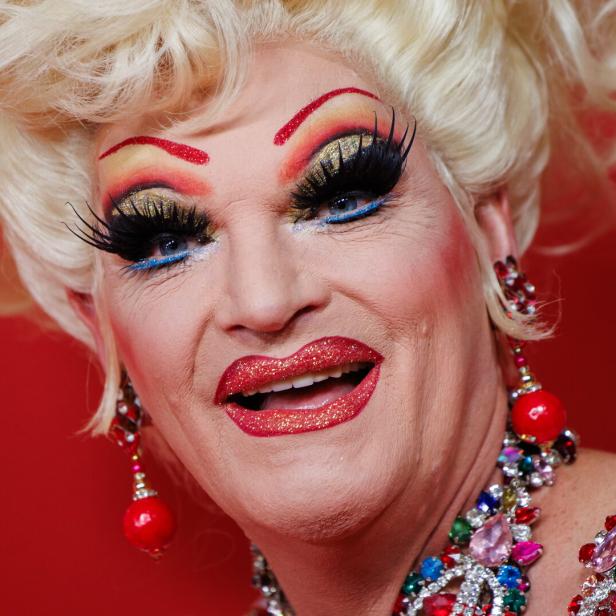 Porträt von Olivia Jones mit auffälligem Make-up und rotem Hintergrund.