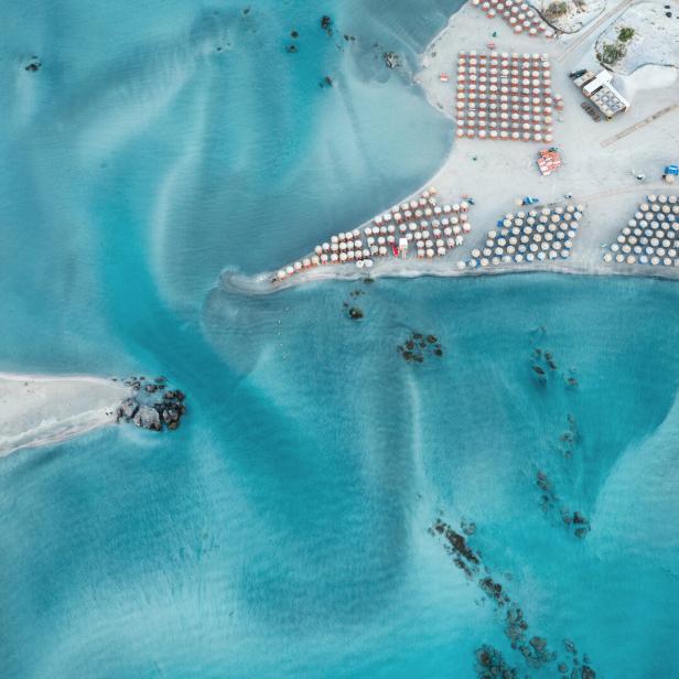 Luftaufnahme des Strandes von Elafonisi, Kreta, mit türkisfarbenem Wasser und Sonnenschirmen.