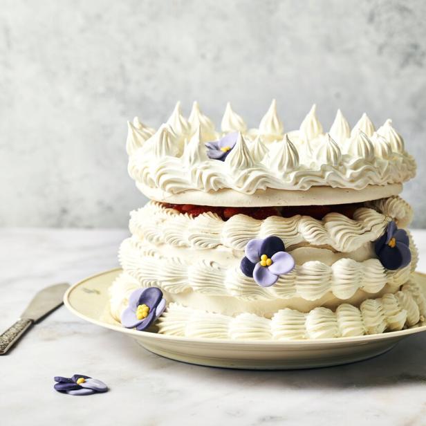 Eine zweistöckige Torte mit weißer Creme und lila Blüten auf einem Teller.