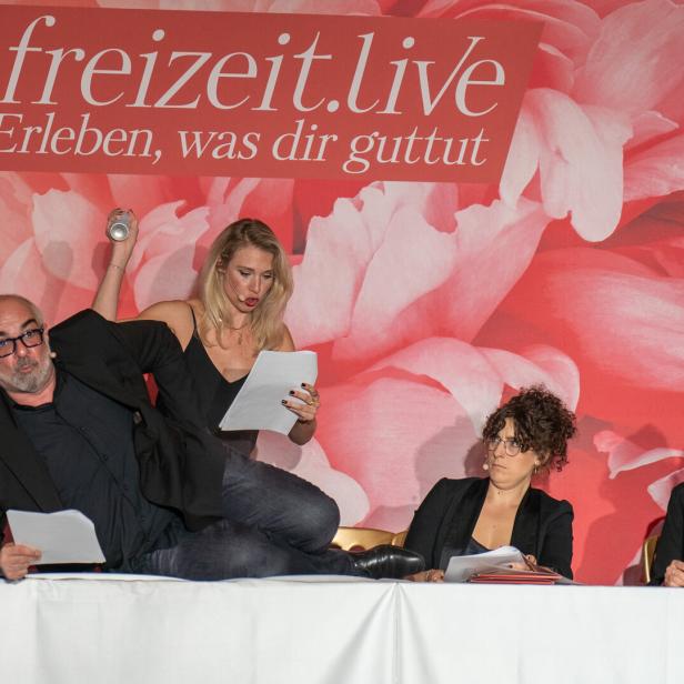 Eine Gruppe von Personen sitzt an einem Tisch vor einem Banner von freizeit.live.