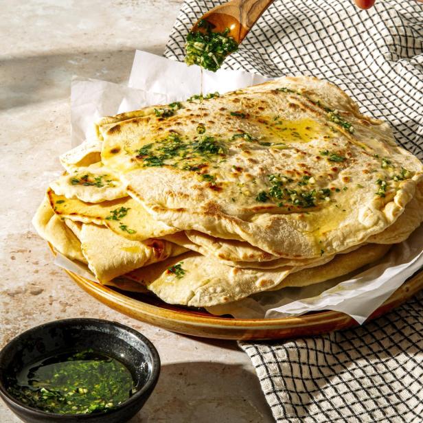 Ein Stapel Fladenbrot wird mit einer Kräuter-Öl-Mischung beträufelt.