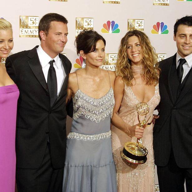 Die Besetzung von „Friends“ posiert mit Jennifer Aniston, die eine Emmy-Trophäe hält.