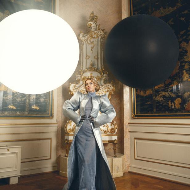 Kiera Chaplin posiert in einem eleganten, silberfarbenen Kleid in einem prunkvollen Raum.