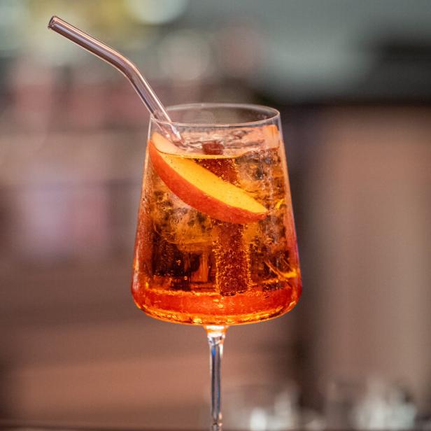 Ein Aperol Spritz mit einem Apfelstück und einem Trinkhalm in einem Glas.