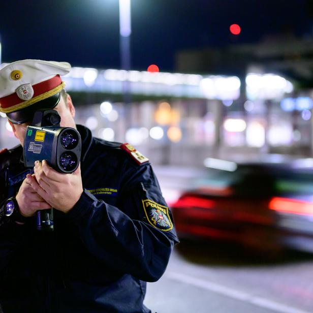 Ein Polizist misst mit einer Laserpistole die Geschwindigkeit eines vorbeifahrenden Autos.