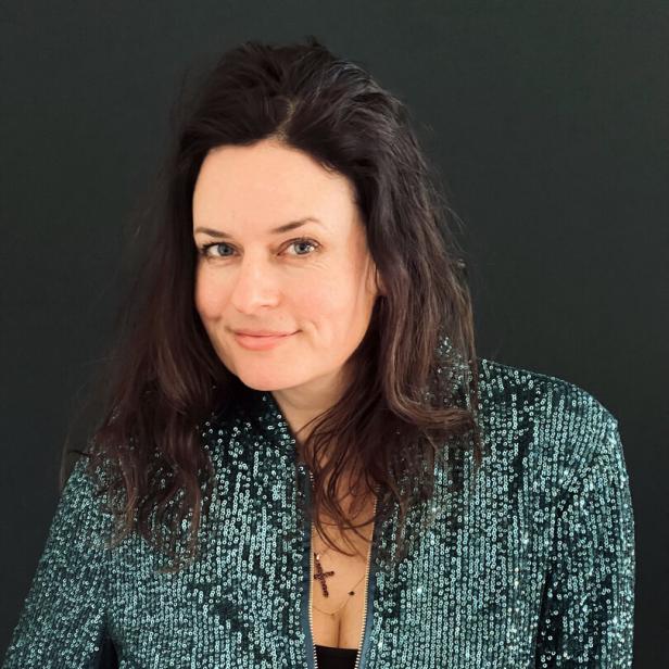 Eine Frau mit dunklen Haaren trägt eine glitzernde, grüne Jacke.