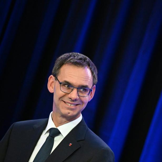 Ein lächelnder Mann mit Brille vor einem blauen Hintergrund.