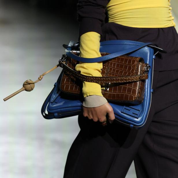 Eine Person trägt eine blaue Handtasche mit einer braunen Tasche aus Krokodilleder darüber.