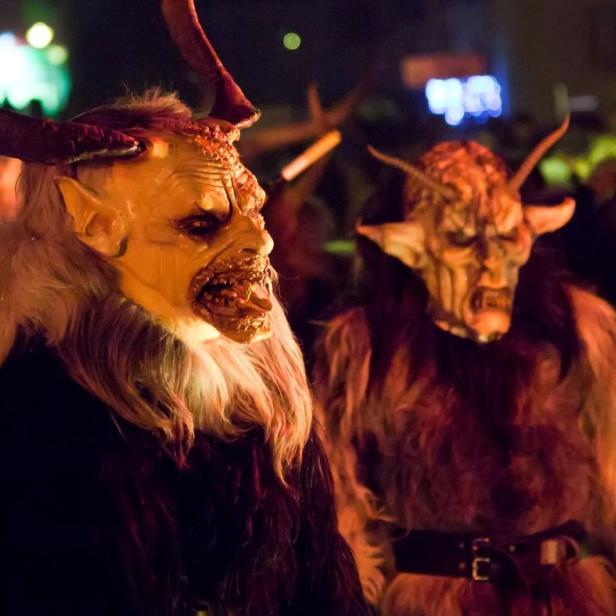 Drei Krampusse mit furchteinflößenden Masken und Hörnern stehen in einer Menschenmenge.
