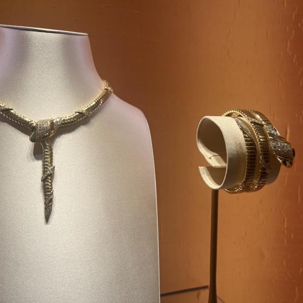 Eine goldene Schlangenhalskette und ein Armband auf Schmuckständern.