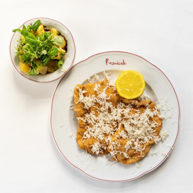 Ein Teller mit Wiener Schnitzel, garniert mit Zitrone und Kartoffelsalat.